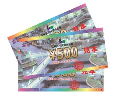 商品券の見本。お札のような形で上辺・下辺は虹色の帯入り、背景にはクローバー橋の写真が入り、中央に500円と記載ある