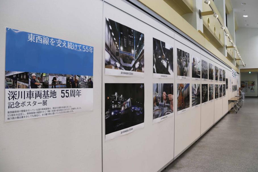 文化センターの白い壁に上下二列に貼られた55周年記念ポスター19点。夜の車両基地や、点検中の車両の写真などが並ぶ。