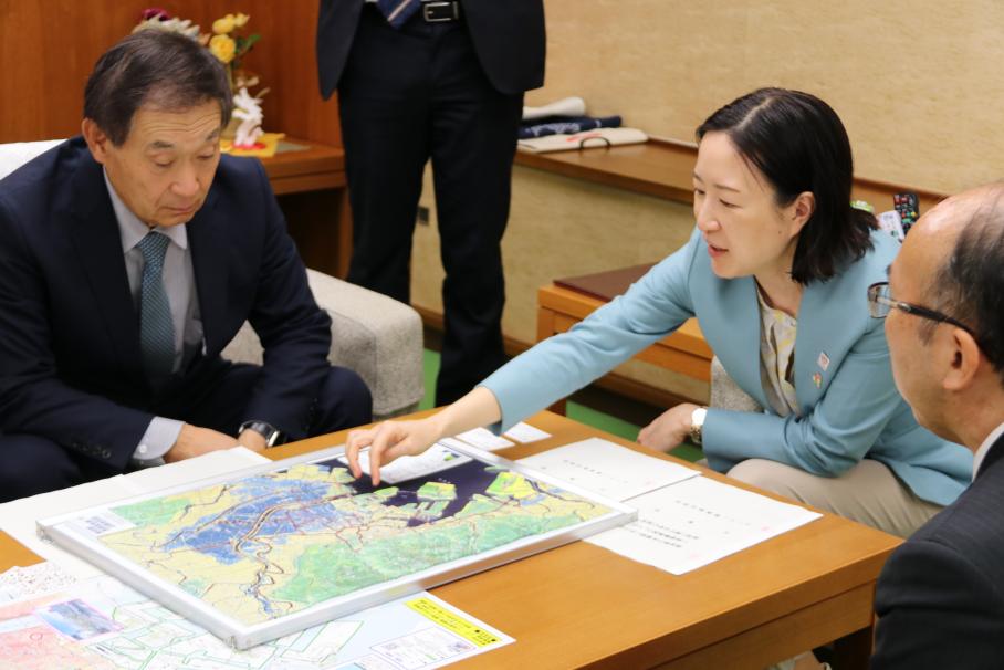机に置かれた江東区の立体地図を指さし、水害について話す区長と、地図を覗き見る疋田社長。