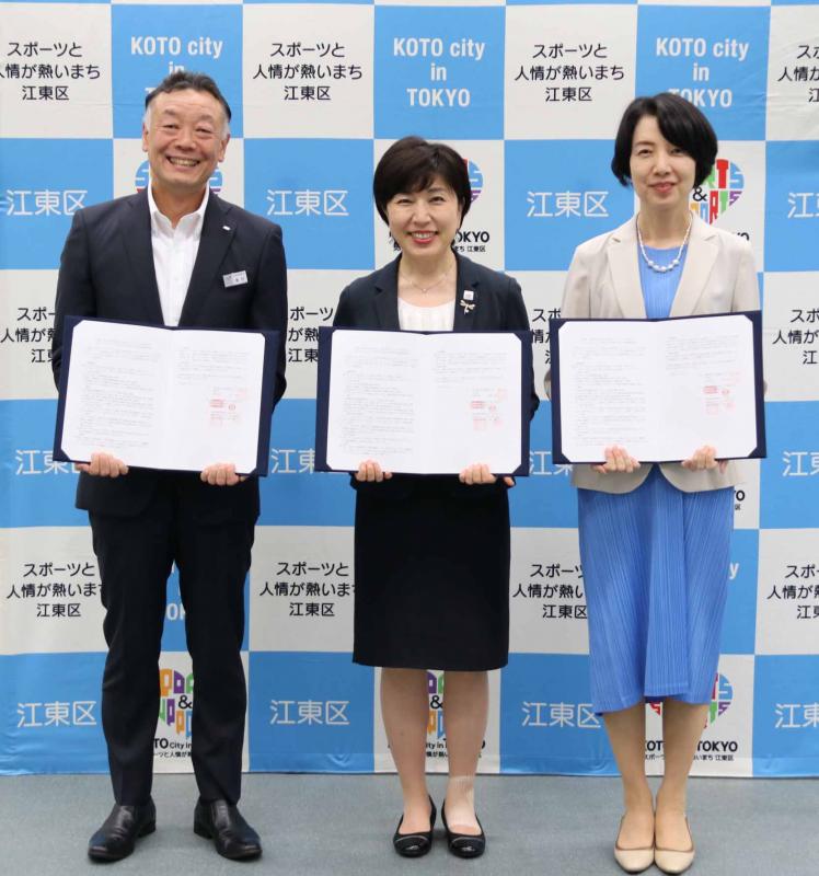 3者の押印を行った協定書を手に持ち、見開いて中身を見せ、笑顔で立つ東京ガスネットワーク奥村取締役、木村区長、東京ガス小西執行役員