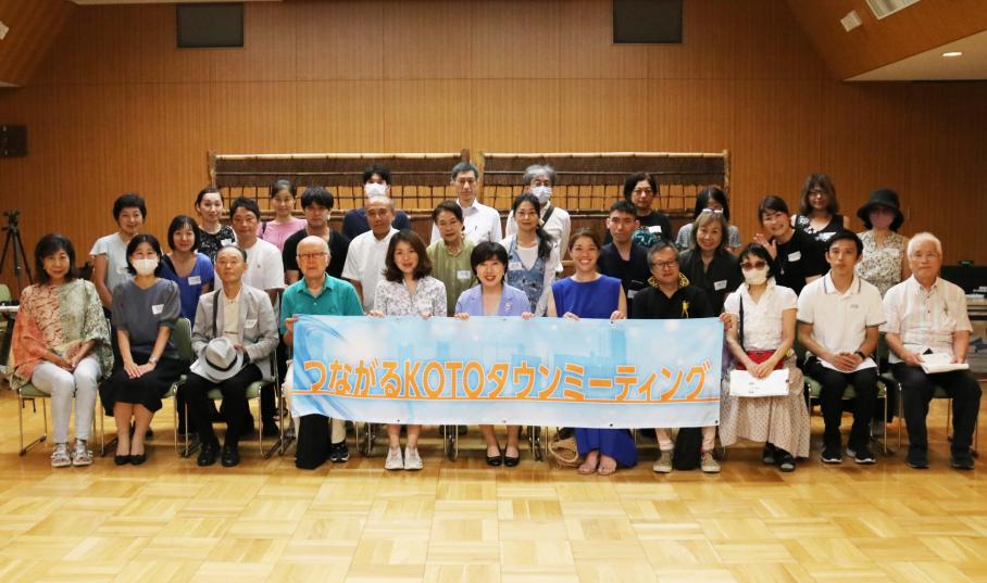 水色の背景にオレンジで「つながるこうとうタウンミーティング」と記載された旗を手に持ちうつる、木村区長と参加者約30名。