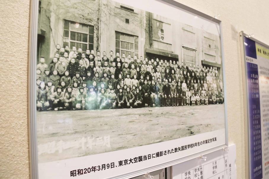 東京大空襲当日に撮影された卒業記念写真。卒業を喜ぶかのような笑顔のこども達と教師が校舎の前のひな壇に立ち、集合している。