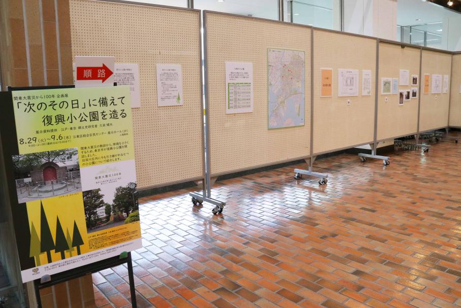 左に企画展のタイトルが記載された黄緑色にオレンジの看板があり、奥には復興小公園の開設パネル、江東区の地図、写真等が展示されている