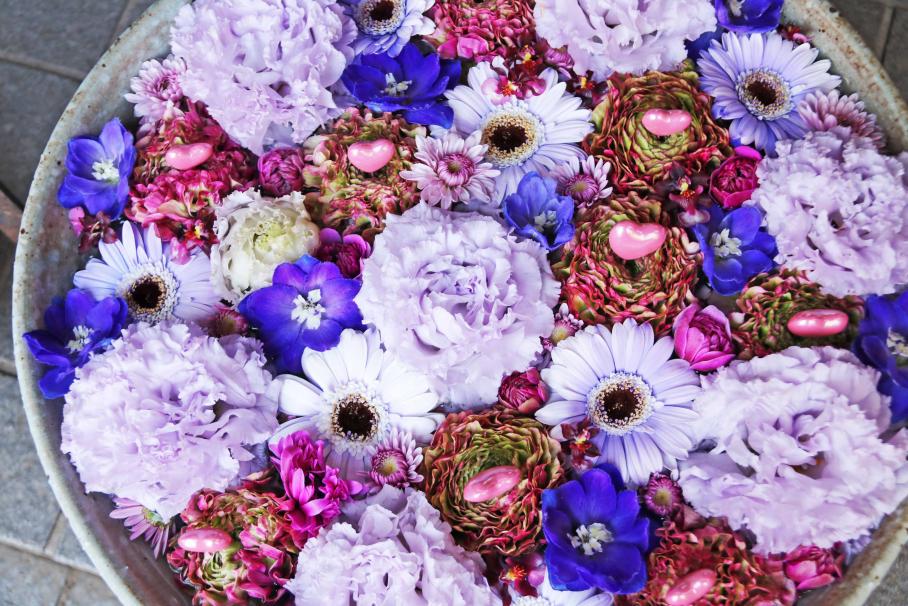 丸い鉢の中を薄紫色のカーネーションやガーベラ、青い花、ピンクと緑の混じった花などが埋め尽くしている